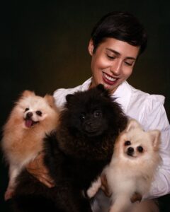 Happy woman holding three adorable Pomeranian dogs, radiating joy and warmth.
