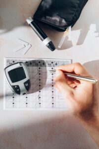 Close-up of a diabetes management kit including a glucometer, lancet pen, and recording sheet on a white table.