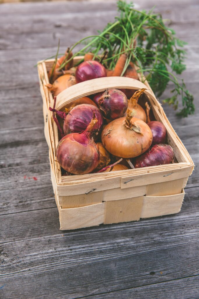 A rustic basket filled with fresh carrots and onions on a wooden table, capturing the essence of harvest season.