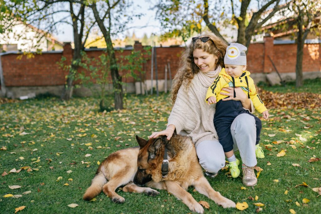 Mother and son enjoy a fall day outdoors with their German Shepherd dog, surrounded by autumn leaves.
