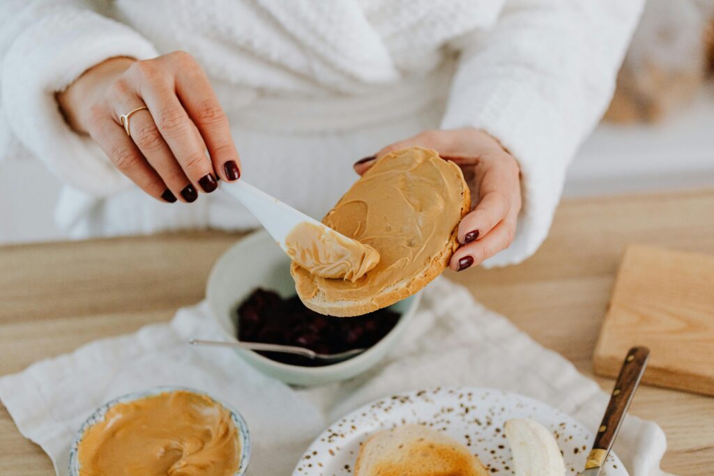 Close-up of a woman spreading creamy peanut butter on toast, perfect for breakfast.